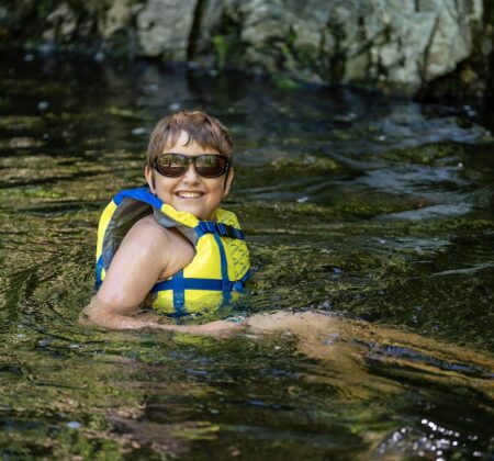 Kid smiling in river wearing life jacket. Photo by Evan Kay