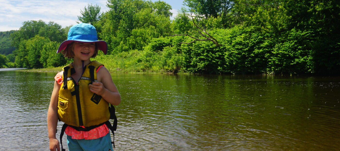 Kid smiling and swimming at the Poland Covered Bridge, a swim spot on the Lamoille River, during Vermont summertime