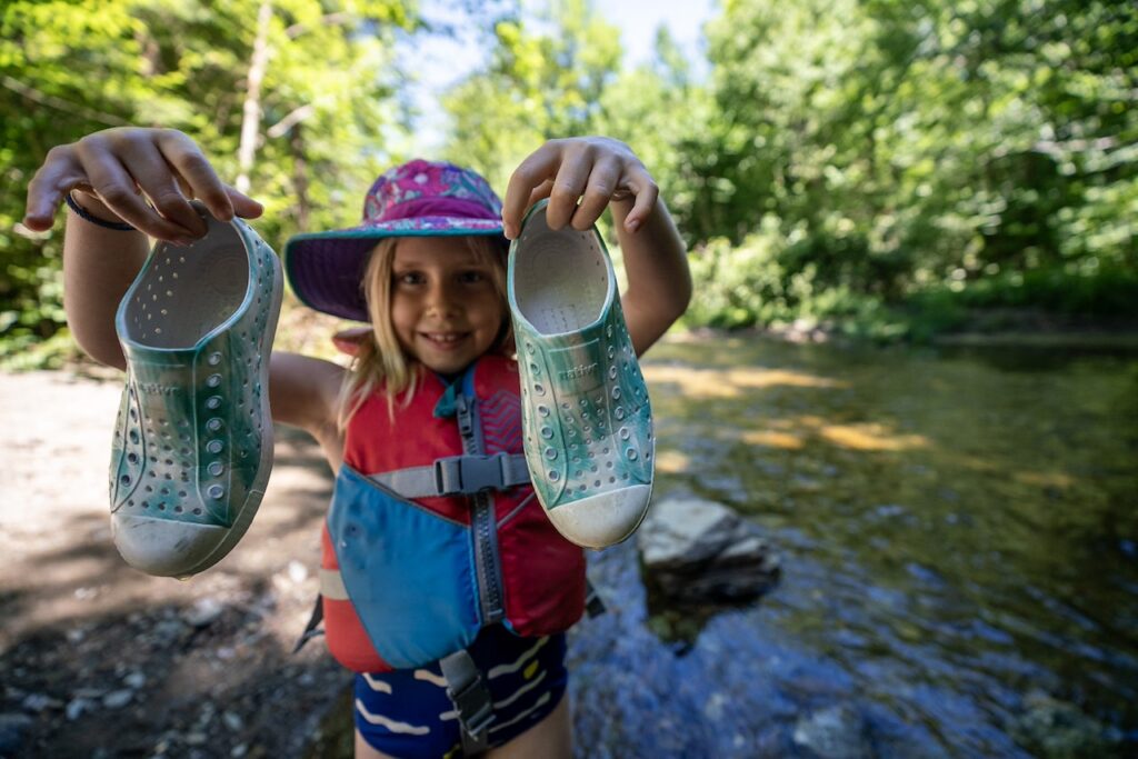 Child wearing lifejacket holding up watershoes Pc. Evan Kay