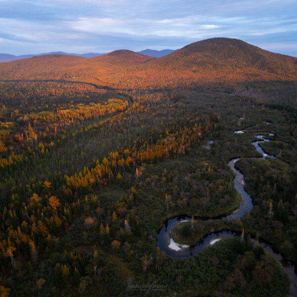 Mountain landscape in autumn fall with a winding headwater river meandering through the valley, surrounded by colorful fall foliage and illuminated by warm alpenglow photographed by Emanuel Soza Foias