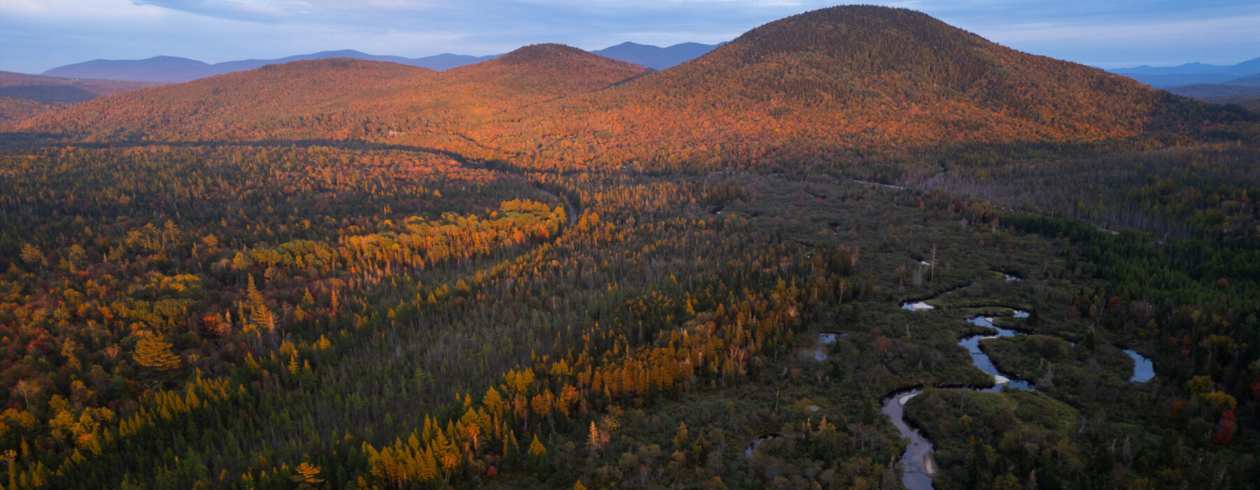Mountain landscape in autumn fall with a winding headwater river meandering through the valley, surrounded by colorful fall foliage and illuminated by warm alpenglow photographed by Emanuel Soza Foias