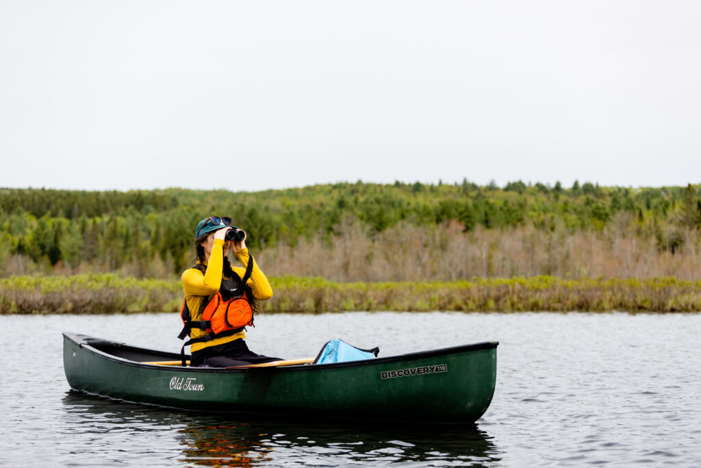 Woman holding binoculars while birdwatching along the Clyde River during World Fish Migration Day on May 23, 2026, in East Charleston, Vermont. Photo by Evan L'Roy.