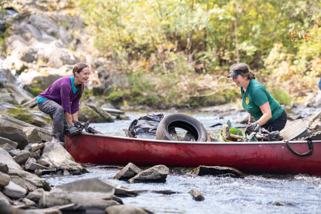 Two woman cleaning up river trash with a canoe in Vermont