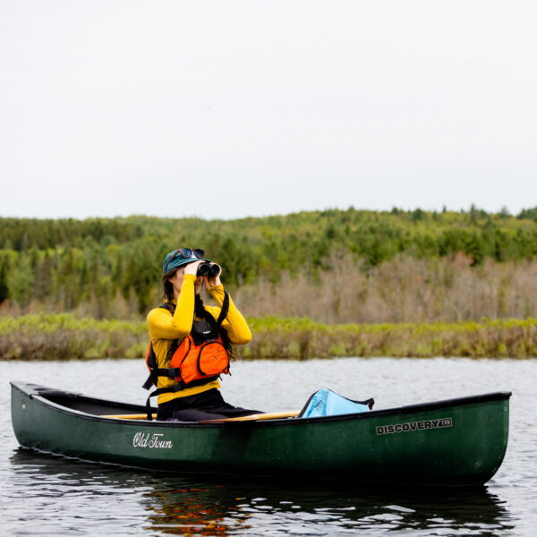 Woman holding binoculars while birdwatching canoe paddle event along the Clyde River during World Fish Migration Day on May 23, 2026, in East Charleston, Vermont. Photo by Evan L'Roy.